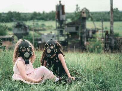 A group of children in gas masks rest on the grass, surrounded by the eerie glow of a nearby contaminated forest