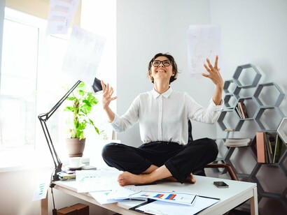 A professional sits cross-legged on a cluttered desk, joyfully tossing papers into the air—a moment of emotional release that reflects the law of interaction, where accumulated work stress transforms into a burst of liberating energy