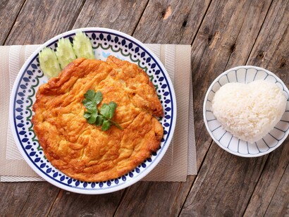 A Thai omelette is served with heart-shaped rice on a rustic wooden table