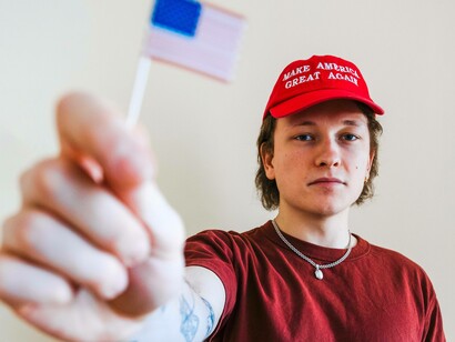 A trump supporter waving a mini American flag and wearing the MAGA hat