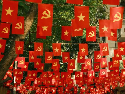 Bandeiras com símbolos comunistas são exibidas em uma via urbana constituindo uma espécie de decoração do espaço público. No artigo, a imagem dialoga com a reflexão sobre ideologias políticas, discursos e os rumos que o autor enxerga para a sociedade brasileira e clama por honestidade