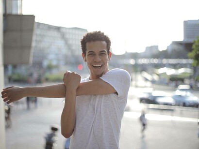 A man smiling and stretching his arm prior to exercising 