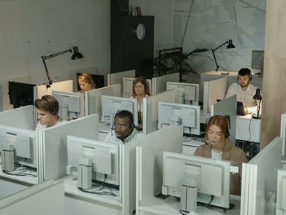 Em um escritório de atendimento, trabalhadores ocupam diferentes postos diante dos computadores. A cena revela a dimensão humana por trás de uma atividade que, para quem está do outro lado da linha, pode parecer reduzida a uma simples voz