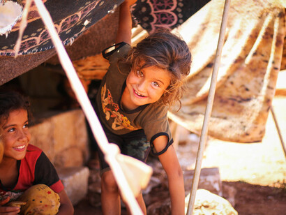 In the dust and cold of a refugee camp, a Kurdish child faces the camera, her eyes reflecting the trauma of war and the weight of a struggle she was born into