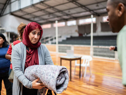 A mature Middle Eastern woman receiving a blanket from a volunteer at a shelter