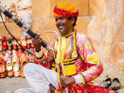 A man dressed in traditional Rajasthani clothing playing a musical instrument, accompanied by the sounds of folk music from India