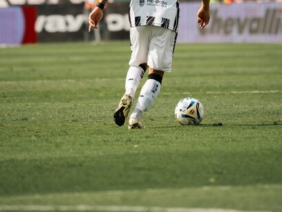 Visto por trás, um jogador com a camisa alvinegra avança com a bola pelo campo. A imagem remete à preparação e à tomada de decisões que fazem parte de uma partida de futebol. Para Gabigol, recuperar o bom desempenho dependerá também de sua capacidade de participar ativamente das jogadas e corresponder às expectativas da equipe