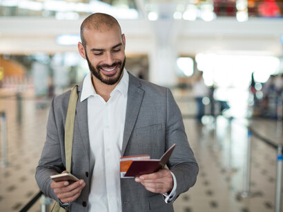 Businessman holding a boarding pass and checking his mobile phone
