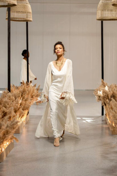 In a vision of sophistication, a model graces the runway in a flowing white creation, highlighting the enduring allure of high-end fashion amidst economic and environmental challenges