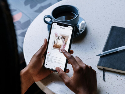 While sitting at a café table, a person scrolls through social media on their black iPhone
