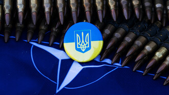 Escudo nacional de Ucrania encima de la bandera de la OTAN, rodeados de munición militar