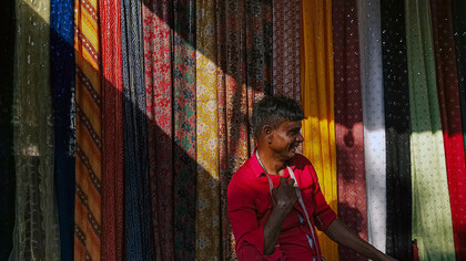 Man measuring fabrics at a market stall in India, selling textiles with care and precision