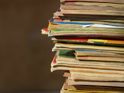 A dense pile of magazines reflects how Ramparts Magazine exposed the hidden ties between media, advertising, and power