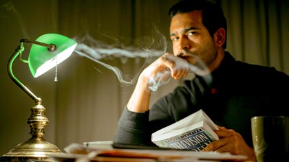 Homem pensativo com livro sentado em quarto esperando a inspiração