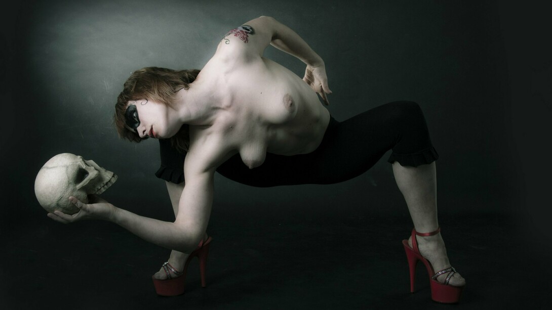 Uma pessoa de maquiagem dramática inclina o corpo em uma pose teatral, segurando uma caveira junto ao chão. A imagem evoca a presença da morte e dialoga com a reflexão do artigo sobre a finitude humana e a passagem do tempo