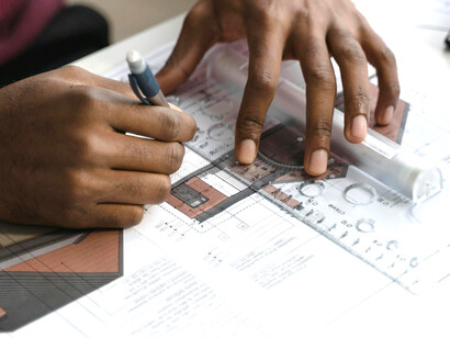 An architecture student studying and designing by hand, carefully drawing blueprints at their desk