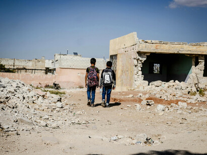 Students walking on an unpaved road through the ruins of a war-torn city, Idlib, Idlib Governorate, Syria