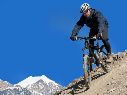 A cyclist rides along the Annapurna Circuit in the Himalayas of Nepal, surrounded by dramatic mountain landscape