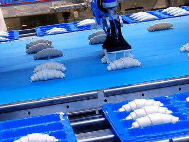 Automated robotic systems transfer semi-finished products from conveyor belts into containers, streamlining the mass production of French croissants