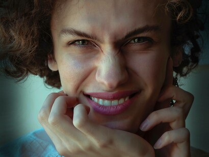 A trans woman who is part of the LBGTQ+ community is smiling and wincing her eyes