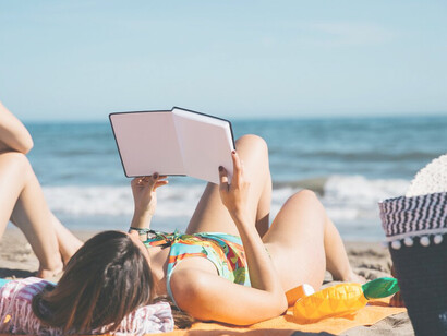 At the beach, a woman and her friend indulge in a digital detox, surrounded by nature and travel, peacefully reading a book