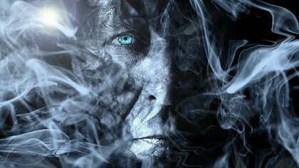 A face shrouded in smoke, showing a hint of human suffering and vulnerability
