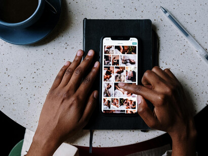 A person relaxes at a café, browsing social media on a black iPhone resting on the table