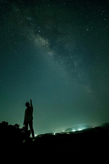 Silhouette of a person pointing at the stars under a clear night sky
