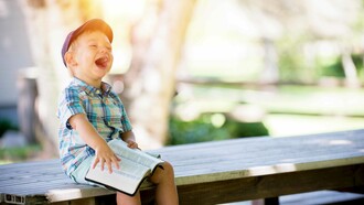 A child barely holding onto his book as he smiles and laughs uncontrollably