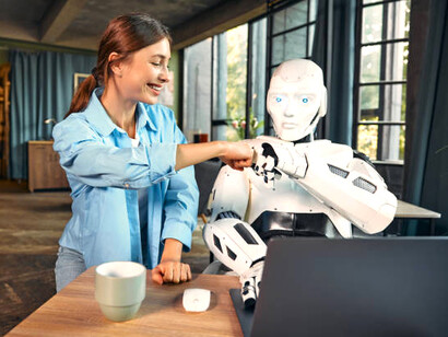 In a modern office, a woman and a robot collaborate at a laptop, capturing the evolving dynamic between human intelligence and artificial intelligenc