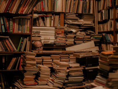 Un hombre tras una pila de libros lee en su biblioteca