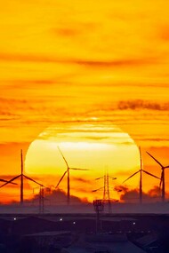 The sun setting in a field of energy-efficient windmills