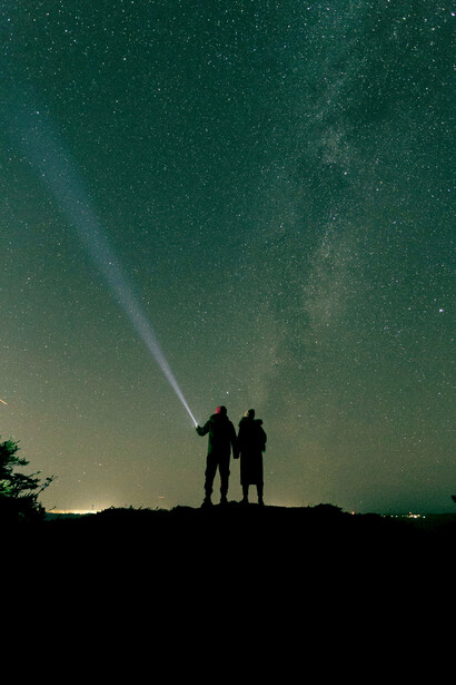 A silhouette of a person standing beneath a starry sky, pointing toward the constellations above