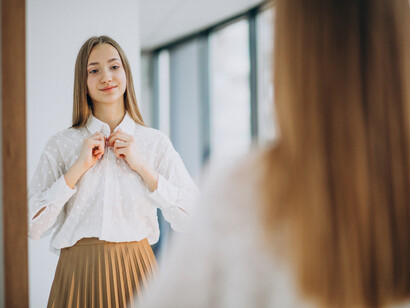 A young woman dressed casually gazes into the mirror, appearing confident