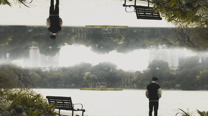 A man standing in front of a park bench, creating an optical illusion that distorts perception