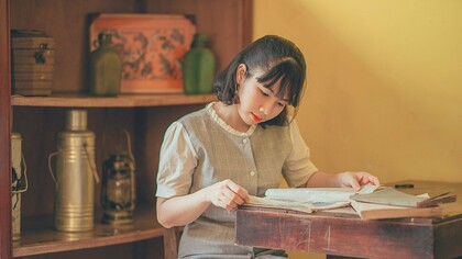 A woman carefully reading aged books at a wooden desk, representing the lifelong pursuit of knowledge through dedicated reading