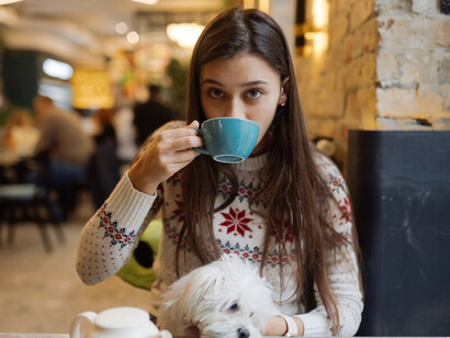 A woman traveling with her pet relaxes in a pet-friendly café, smiling as she holds her cute dog and enjoys a warm cup of coffee