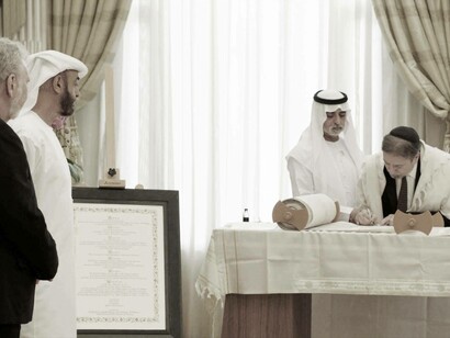 Sheikh Nahayan Mabarak Al Nahayan, UAE Minister of Tolerance and Coexistence, places his hand on the hand of Rabbi Elie Abadie, Senior Rabbi, Jewish Council of the Emirates, as the last letter is written in the Torah Scroll, as H.H. Sheikh Mohamed bin Zayed Al Sultan, John Sexton, President Emeritus, NYU and Co-Founder of NYU Abu Dhabi, look on