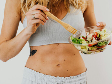 A toned woman eating a vegetable salad and tracking calories for a healthy lifestyle