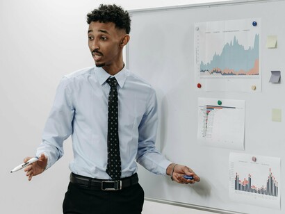 Homem apresenta gráficos e indicadores fixados numa lousa durante explicação técnica. A análise de dados ESG tornou-se essencial para avaliar riscos e atrair investimento sustentável