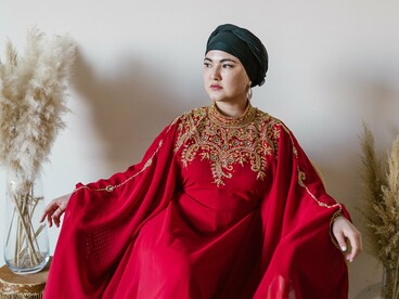 A woman in richly embroidered red traditional attire gazing into the distance, reflecting cultural identity carried through generations