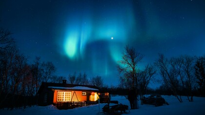 A brown cottage beneath a glowing aurora borealis