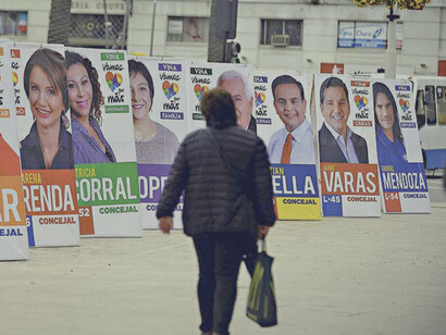 Mujer camina una calle repleta de propaganda electoral en Santiago de Chile