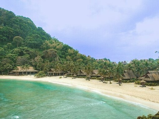 A luxurious island resort, with its pristine beach and lush mountainous backdrop: a form of luxury rooted in material indulgence that contrasts with a "new luxury" focused on transformative experiences and the cultivation of inner states for personal growth