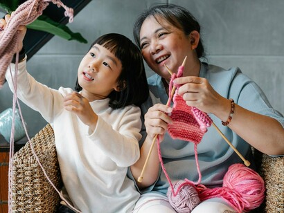 A grandmother patiently teaching her grandchild to knit, representing the passing of culture from one generation to the next