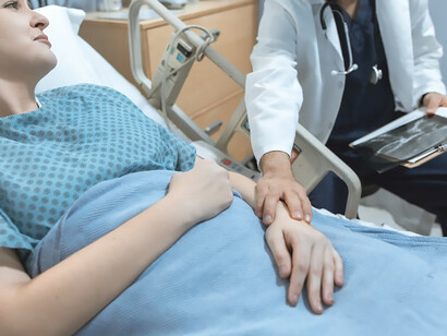 In the confines of a hospital room, a woman, weakened by illness, rests on the bed, her silent tears echoing the weight of her struggle