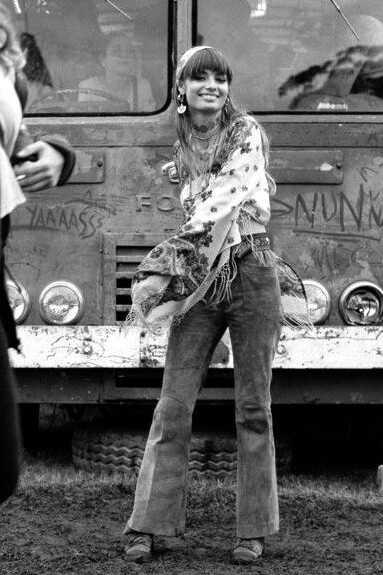 A hippie woman in the 1960s, standing in front of vintage cars, reflecting counterculture fashion and youth rebellion