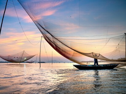 A fisherman lifting his vast nets under a painted dusk sky, representing the invisible bonds that link people to home