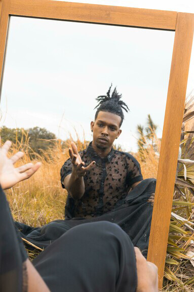A man in a black shirt stands in front of a mirror—capturing a moment of self-expression, identity, and LGBTQ+ visibility online