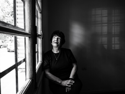Black-and-white portrait of an elderly woman mourning a loved one while gazing through a window in reflective silence